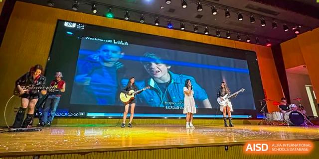 Two students performing on a stage with a large screen behind them at Sino-Canada School.