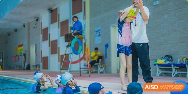 Students in a physical education class, some sitting on a mat while others stand, at Sino-Canada School.