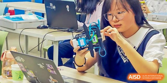 A female student from Suzhou Experimental High School International Center works on a robotics project at her desk.