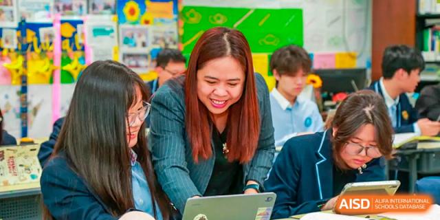 A female teacher from Suzhou Experimental High School International Center smiles and leans in to look at a student's laptop.