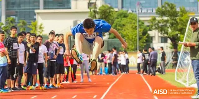 A male student from Suzhou Experimental High School International Center in a blue T-shirt does a long jump on a red track during a sports day.