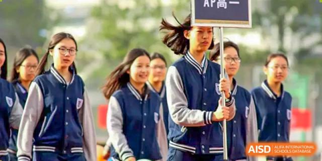 Two students from Suzhou Experimental High School International Center, one wearing a blue and white school jacket, stand at a sports event.