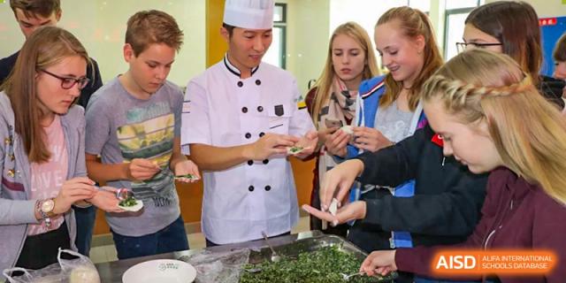 A student from Suzhou Experimental High School International Center in a chef's uniform teaches a group of students how to prepare food.
