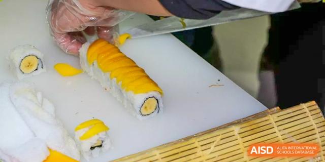 A person from Suzhou Experimental High School International Center prepares a large yellow sushi roll on a cutting board.