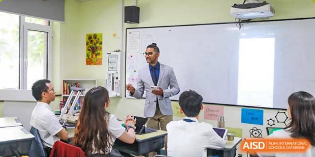 A male teacher is standing in front of students and holding a paper in his hands at The MacDuffie School Tianjin.