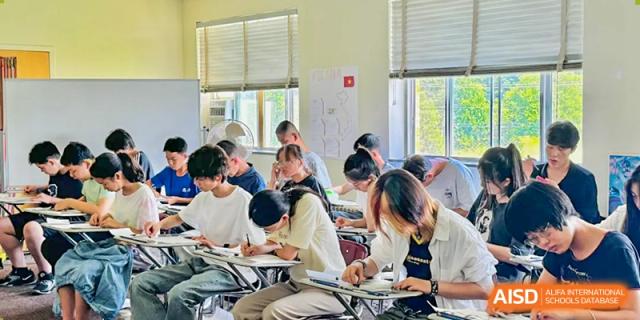A group of students are sitting at desks and writing in their notebooks in a classroom at The MacDuffie School Tianjin.