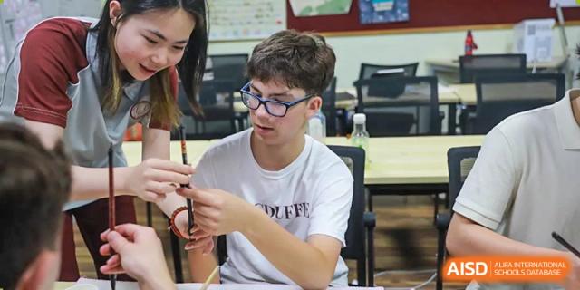 A male student wearing glasses is working on a craft project at The MacDuffie School Tianjin.