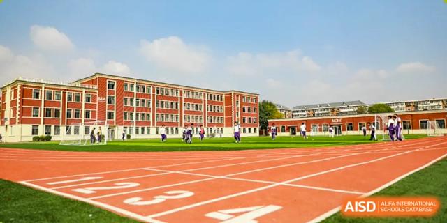 The main building of The MacDuffie School Tianjin with a track and field in the foreground.