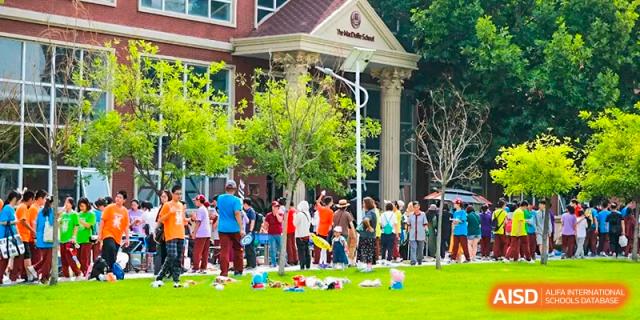 Students from The MacDuffie School Tianjin participate in an outdoor event on a lawn in front of the school building.