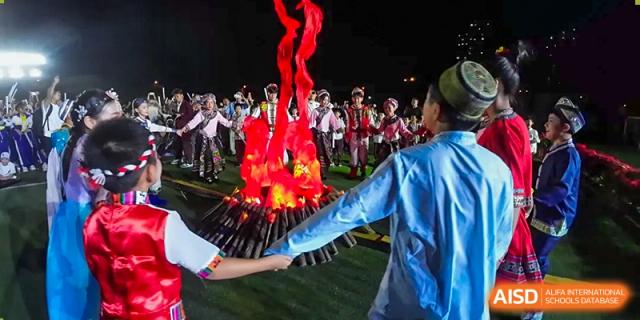 Students and teachers are gathered around a bonfire at night at The MacDuffie School Tianjin.