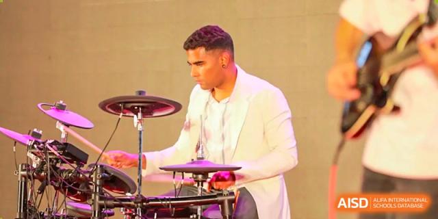 A male student in a white suit is playing the drums on stage at The MacDuffie School Tianjin.