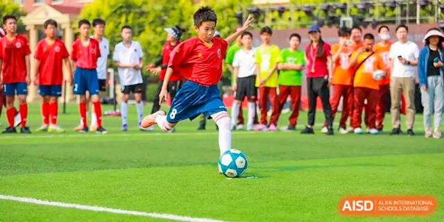A young male student is playing soccer on a grass field during a game at The MacDuffie School Tianjin.