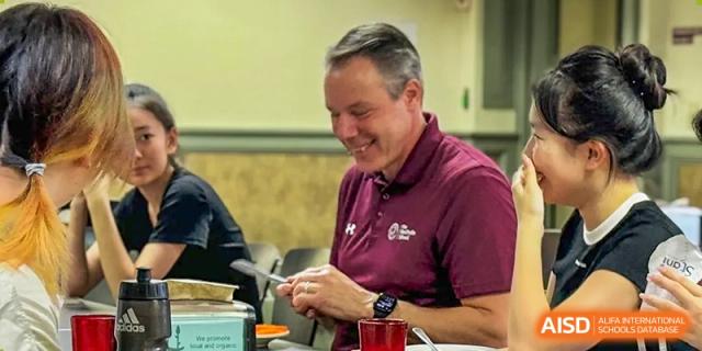 A male teacher is smiling while holding a knife and a plate at The MacDuffie School Tianjin.