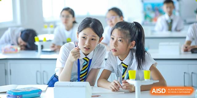 Two Wellington College International Hangzhou students, wearing school uniforms, attentively listening in a classroom.