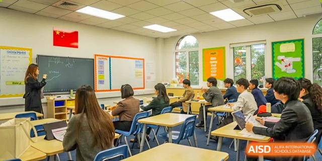 A bright classroom at Wellington College International Hangzhou with students and adults seated at desks, suggesting a small-group lesson or parent/teacher interaction.