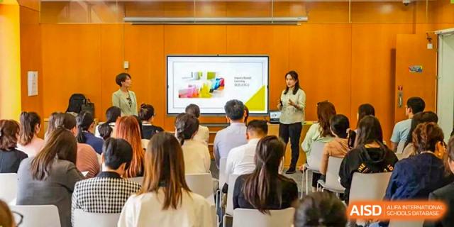 An educator leading a presentation to a group of adults at Wellington College International Hangzhou, with a large screen displaying content.