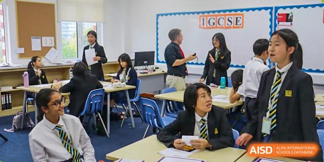 Wellington College International Hangzhou students, wearing uniforms, working at their desks in a classroom, with a teacher visible in the background.