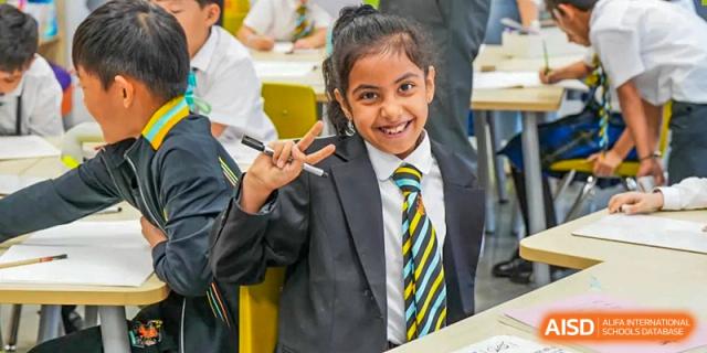 A smiling Wellington College International Hangzhou student in school uniform and tie giving a peace sign, close-up.