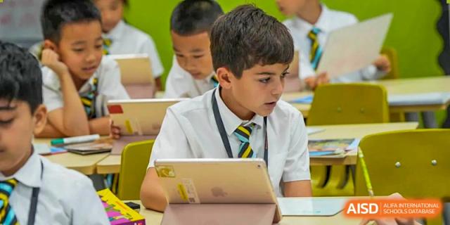 A Wellington College International Hangzhou student in school uniform looking down and working on a digital tablet in the classroom.