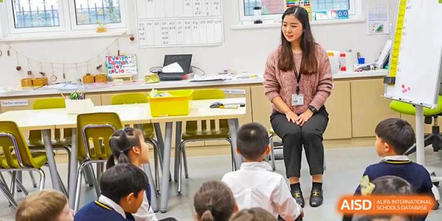 A Wellington College International Hangzhou teacher sitting on a desk and interacting with a group of young students in a classroom setting.