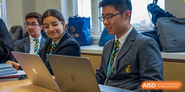 A Wellington College International Hangzhou student, wearing a tie and uniform, smiling while working on a laptop.