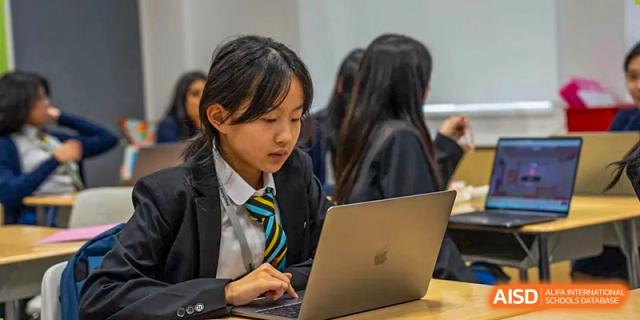 A Wellington College International Hangzhou student intently working on a silver laptop in a classroom.