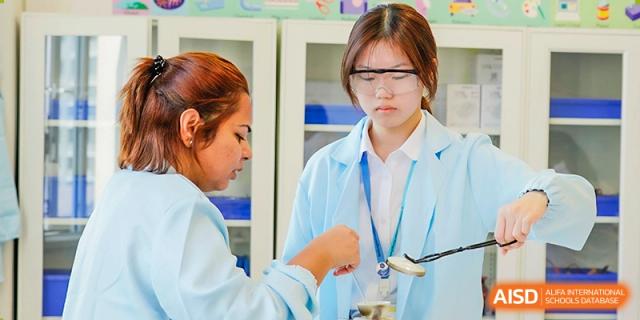 A female Wellington College International Hangzhou student wearing a lab coat and safety goggles, concentrating while performing an experiment in the science lab.