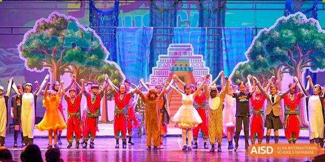 A vibrant musical theater performance with students in colorful costumes, possibly from a show like The Lion King, on a stage. Wellington College International Hangzhou