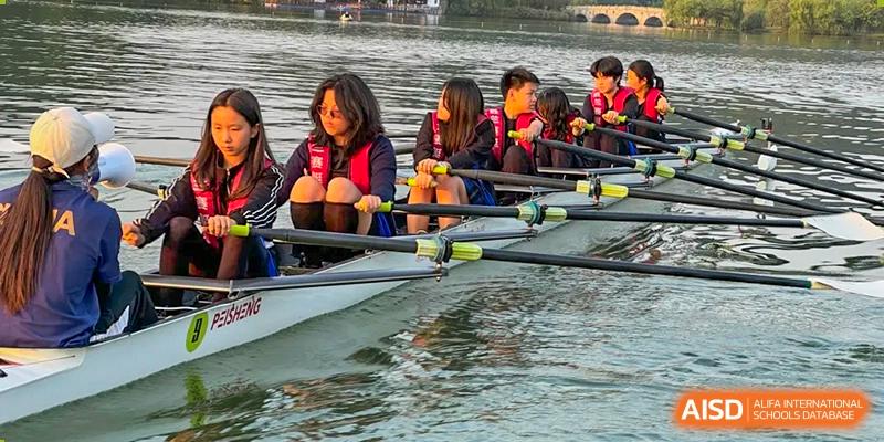 Close-up of students from Wellington College International Hangzhou in life jackets participating in rowing practice on a lake, with their hands on the oars and focused expressions.