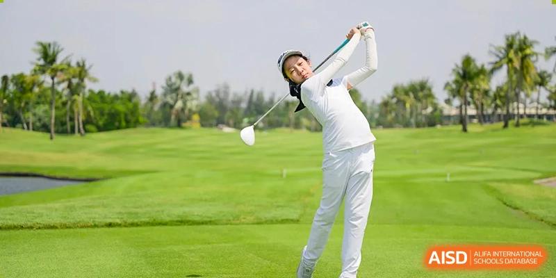 A female student in white golf attire taking a swing on a sunny golf course. Wellington College International Hangzhou