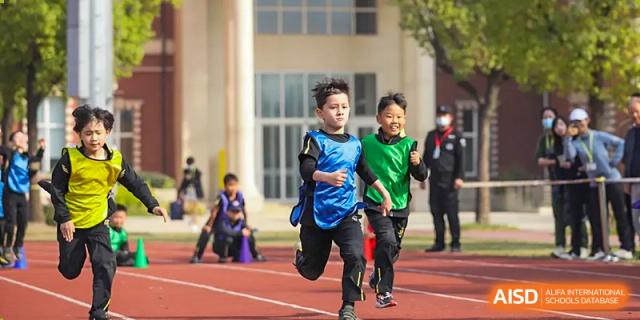 Two young Wellington College International Hangzhou students smiling while running a race on a track, one in a blue vest and the other in a green vest.