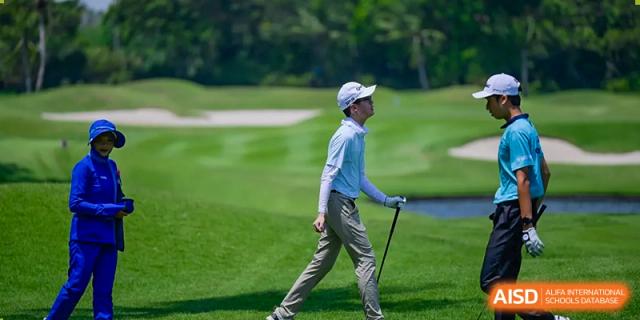 Wellington College International Hangzhou student walking on a lush green golf course, wearing a light blue long-sleeve shirt and cap, holding a golf club.