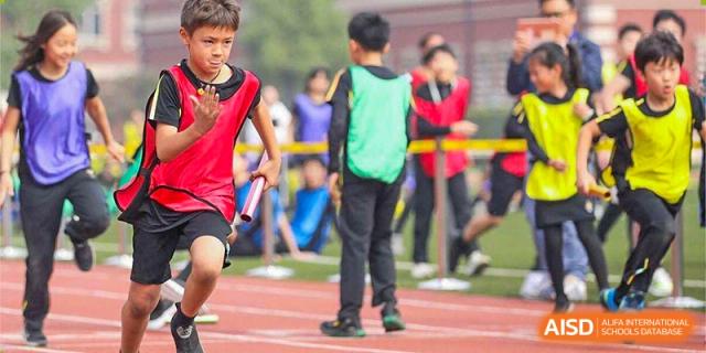 Group of Wellington College International Hangzhou students, some wearing red and others in green sports vests, standing on a field during an outdoor sports event.