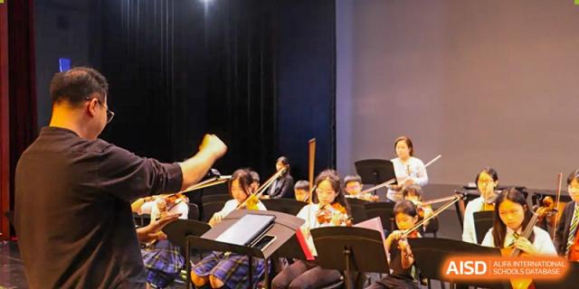 Wellington College International Hangzhou orchestra members playing their instruments on a dark stage during a concert or rehearsal.