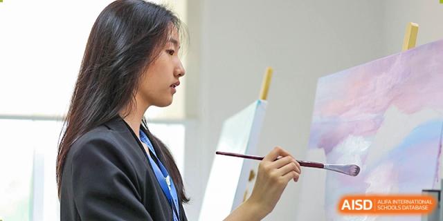 A Wellington College International Hangzhou student focused on painting on a canvas with a brush, showing an art class activity.