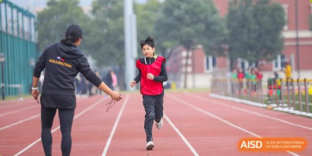 Wellington College International Hangzhou student running enthusiastically in a red sports vest and dark pants on an outdoor running track.