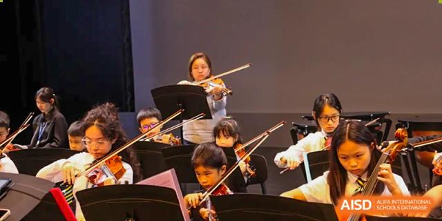 Wellington College International Hangzhou students in an orchestra performing, with a conductor leading them on a stage.