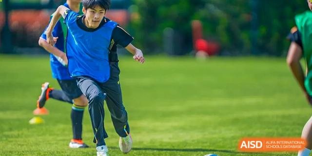 A Wellington College International Hangzhou student running on a green sports field during an outdoor physical education or sports event.