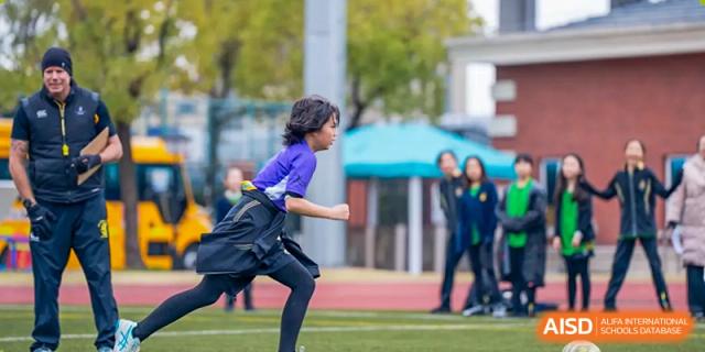 Two Wellington College International Hangzhou students, one in a purple uniform, running toward each other on a sports field.