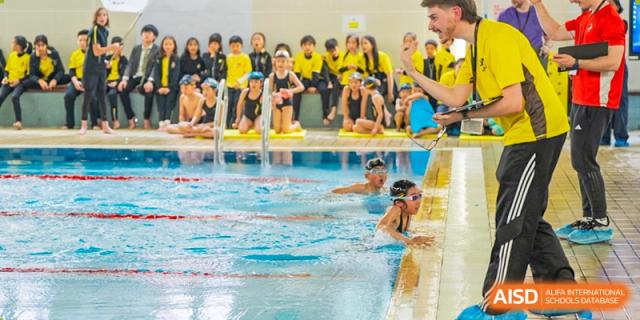 A Wellington College International Hangzhou student swimming laps in the school pool while other students watch from the side.