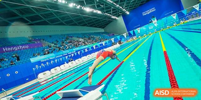 A Wellington College International Hangzhou swimmer mid-dive into the pool from the starting blocks at an indoor swim meet.