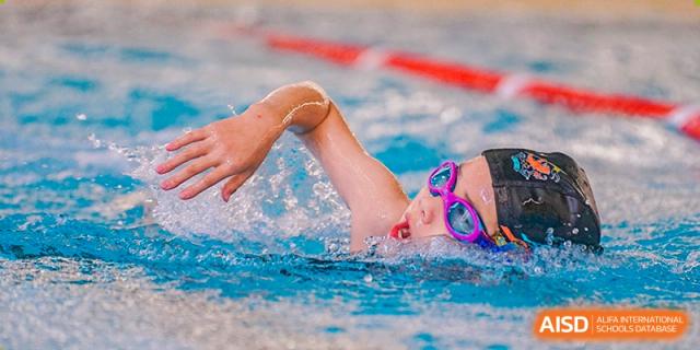 Close-up of a Wellington College International Hangzhou student swimming freestyle, wearing goggles and a swim cap, during a competition or training.