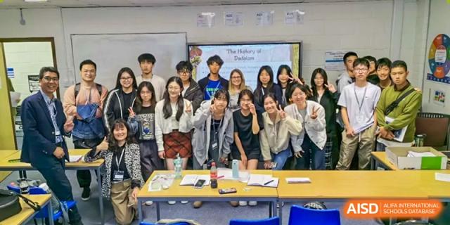 A large group of smiling Zhejiang Wenzhou High School International Division students and teachers posing for a cheerful photo around a classroom table.