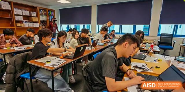 A busy classroom setting at Zhejiang Wenzhou High School International Division with students working on laptops and taking notes at tables.