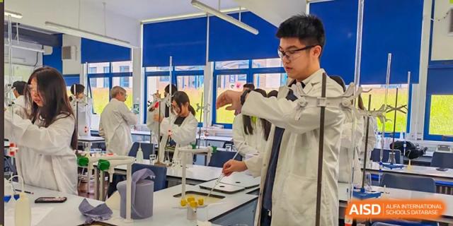 Two Zhejiang Wenzhou High School International Division students in lab coats working together on a chemistry or biology experiment in a bright science lab.