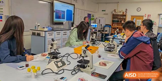 A modern science lab at Zhejiang Wenzhou High School International Division with students working at stations, utilizing microscopes, computers, and other scientific equipment.