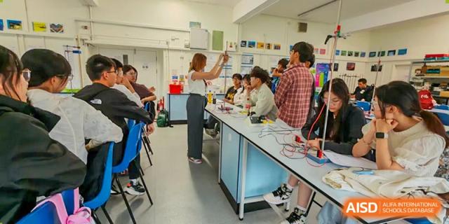 Students from Zhejiang Wenzhou High School International Division conducting a hands-on experiment with wires and power supplies in a bright, modern science laboratory.