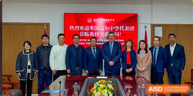 A delegation from Zhejiang Wenzhou High School International Division posing for a group photo with representatives from a partner institution in front of a welcome banner.