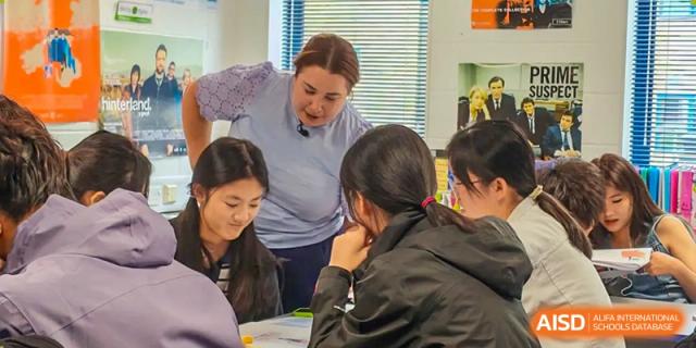 A teacher from Zhejiang Wenzhou High School International Division bending down to assist a small group of students with an assignment or practical task.