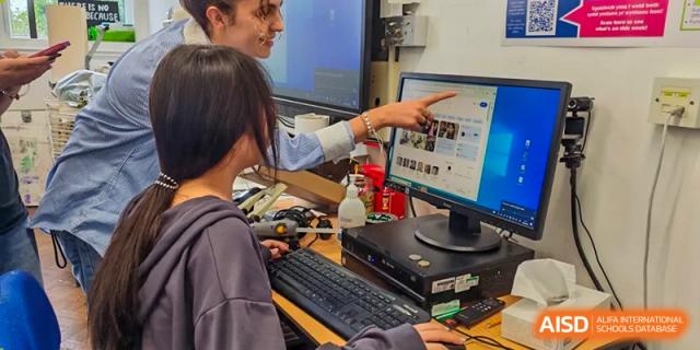 A teacher at Zhejiang Wenzhou High School International Division pointing at information on a computer screen to guide a student working at the keyboard.